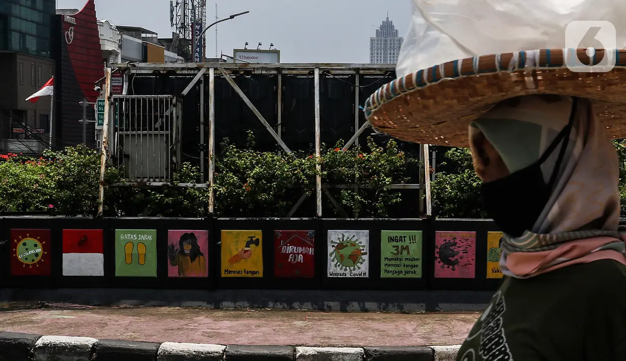 Warga melintasi mural sosialisasi bahaya COVID-19 di Jalan Sultan Iskandar Muda, Jakarta, Rabu (23/9/2020). PSBB pengetatan sepekan terakhir ini belum efektif menurunkan angka jumlah harian Covid-19 di DKI yang tercatat bertambah 1.122 kasus di ibu kota pada Selasa (22/9). (Liputan6.com/Johan Tallo)