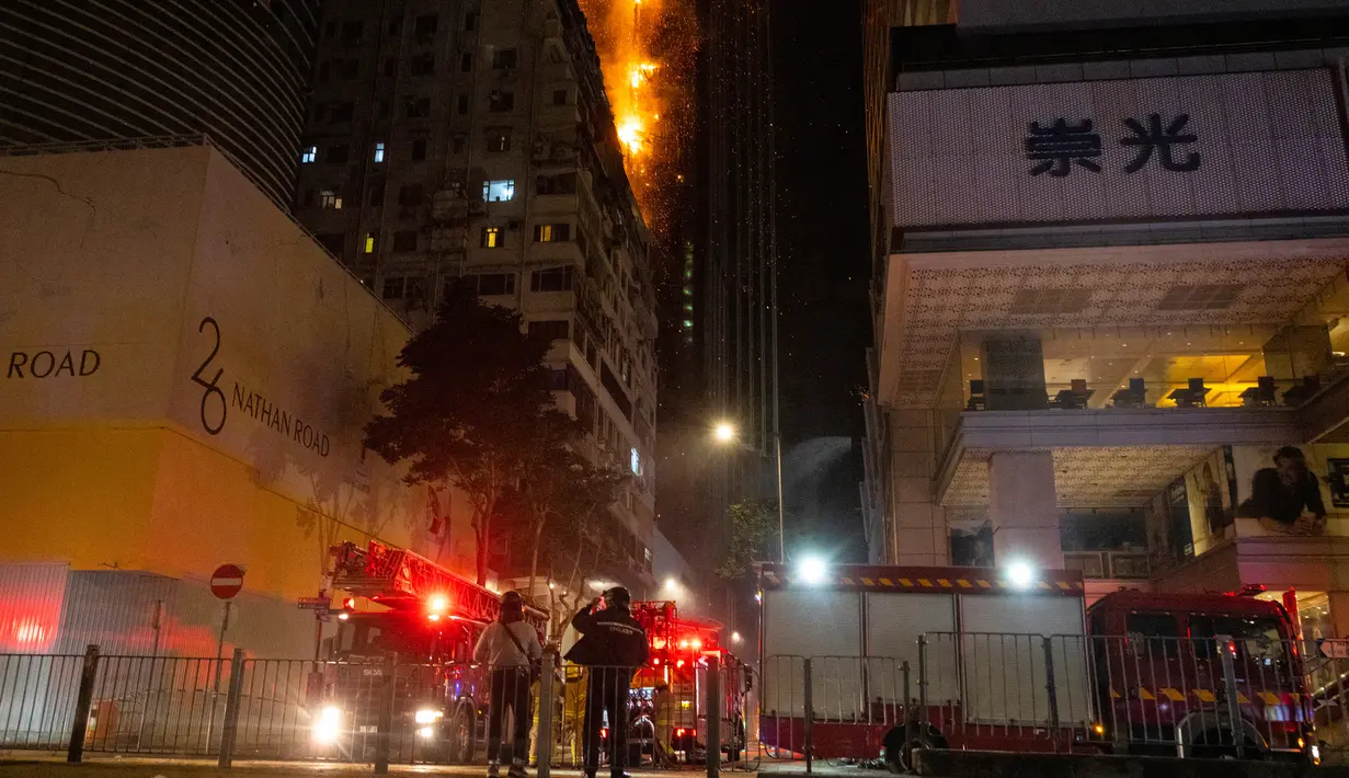Petugas pemadam kebakaran memadamkan api di lokasi konstruksi di Hong Kong, Jumat (3/3/2023). Petugas pemadam kebakaran dan truk pemadam kebakaran terlihat di jalan-jalan di dekatnya saat api membubung dari atas gedung yang terbakar. (AP Photo/Louise Delmotte)