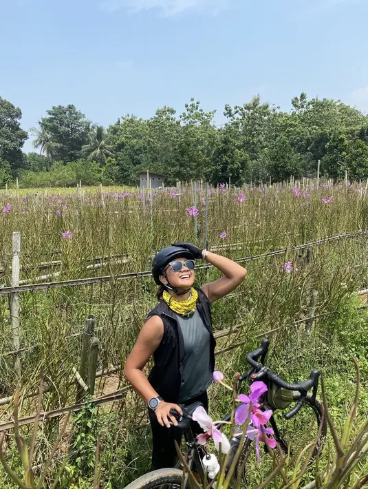 Saat bersepeda, Nirina Zubir tak sengaja pamer lengan berotot di tengah kebun anggrek. Ia mengenakan tanktop dan vest hitam [@nirinazubir_]