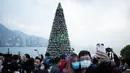 Sepasang kekasih berpose di depan pohon Natal raksasa saat Natal di distrik budaya West Kowloon di Hong Kong (25/12/2021). Pohon Natal raksasa ini memiliki ukuran setinggi 20 meter. (AFP/Bertha Wang)