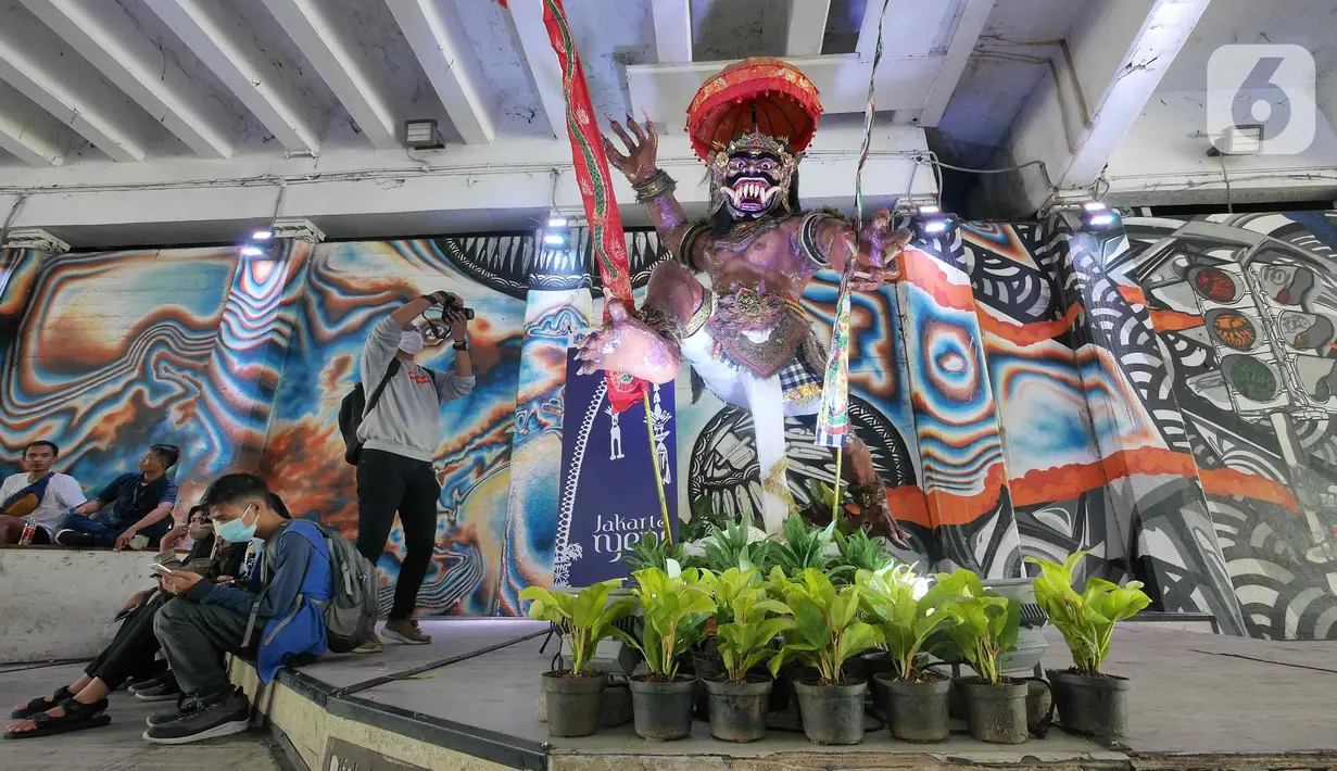 Warga beraktivitas di depan instalasi Ogoh-ogoh di Terowongan Kendal, Jakarta, Senin (28/2/2022). Pemprov DKI Jakarta menampilkan instalasi Ogoh-ogoh di beberapa titik di Jakarta, seperti di Stasiun Tebet, Terowongan Kendal dan Halte CSW menyambut Hari Raya Nyepi 2022. (Liputan6.com/Herman Zakharia)