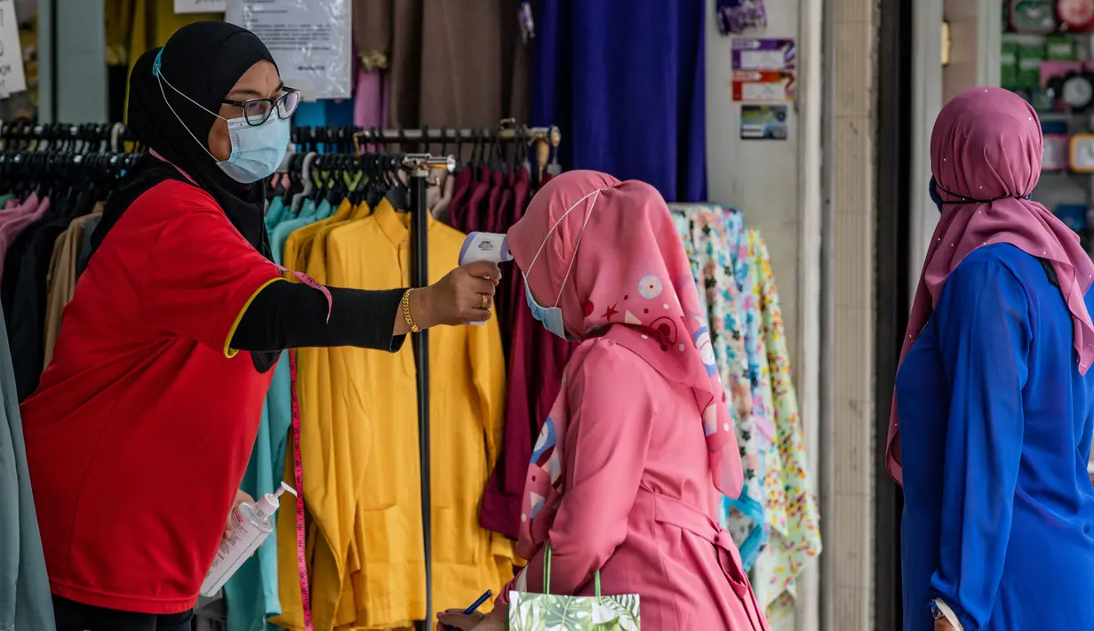 Pekerja memeriksa suhu seorang wanita Muslim, sebagai tindakan pencegahan penyebaran Covid-19 sebelum memasuki toko yang menjual pakaian budaya Malaysia atau baju melayu dan baju kurung menjelang Idul Fitri yang menandai berakhirnya bulan suci Ramadan di Kuala Lumpur (13/5/2020). (AFP/Mohd Rasfan)