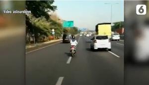 Seorang wanita berhijab dengan skuter matik melintasi jalan tol