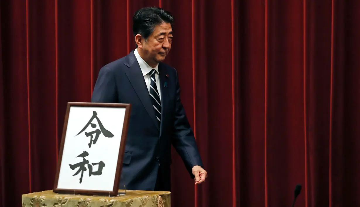 Perdana Menteri Jepang, Shinzo Abe berjalan melintasi plakat nama era baru Kekaisaran Jepang, Reiwa, seusai konferensi pers di Tokyo, Senin (1/4). Reiwa menjadi nama era yang baru yang mengganti Era Heisei seiring persiapan pengunduran diri Kaisar Akihito pada 31 April mendatang. (AP/Eugene Hoshiko)