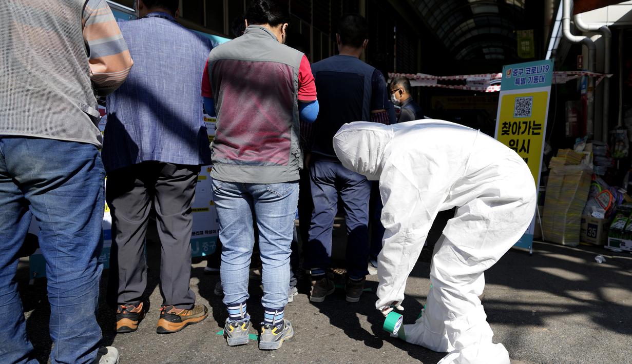 Seorang pekerja medis yang mengenakan alat pelindung menempelkan tanda-tanda untuk langkah-langkah jarak sosial dan tindakan pencegahan terhadap virus corona saat orang mengantre untuk menunggu untuk mendapatkan tes virus corona di Seoul, Korea Selatan, Jumat (24/9/2021). (AP Photo/Lee Jin-man)