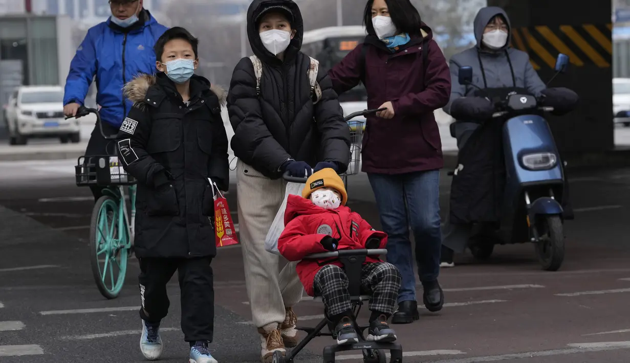 Seorang anak dengan masker didorong menyeberang jalan di Beijing, China, Jumat (2/12/2022). Lebih banyak kota melonggarkan pembatasan, memungkinkan pusat perbelanjaan, supermarket, dan bisnis lainnya dibuka kembali menyusul protes akhir pekan lalu di Shanghai dan daerah lain di mana beberapa orang menyerukan Presiden Xi Jinping untuk mengundurkan diri. (AP Photo/Ng Han Guan)