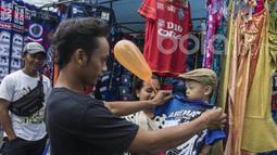 Seorang bapak mencobakan anaknya baju yang dijual oleh pedagang kaki lima jelang laga semifinal Piala Presiden 2017 antara Arema FC melawan Semen Padang di sekitar Stadion Kanjuruhan, Malang, Jawa Timur, Minggu (5/3/2017). (Bola.com/Vitalis Yogi Trisna)
