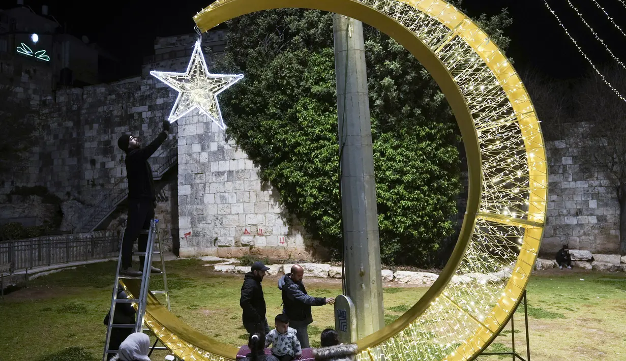 Seorang pria Palestina menggantungkan lampu hias untuk menyambut bulan suci Ramadhan, tepat di luar Kota Tua Yerusalem, Selasa, 21 Maret 2023. (AP Photo/Mahmoud Illean)
