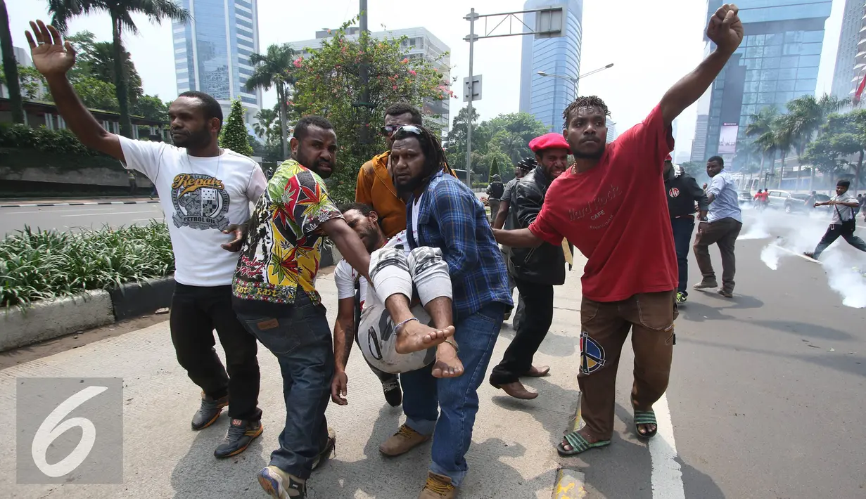 Mahasiswa menolong temannya yang terkapar saat aksi perayaan ekspresi identitas Papua di Jakarta, Selasa (1/12). Puluhan massa aksi diamankan dalam aksi tersebut sementara beberapa lainnya mengalami luka akibat bentrokan. (Liputan6.com/Immanuel Antonius)