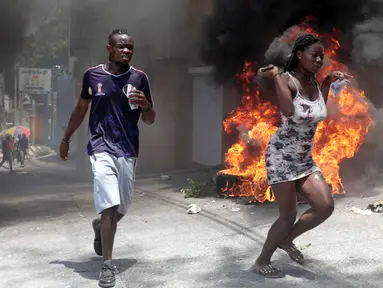 Demonstran berlari melewati ban yang dibakar selama protes terhadap ketidakamanan di Port-au-Prince, Haiti, Senin (7/8/2023). Ribuan warga Haiti turun ke jalan-jalan Port-au-Prince untuk memprotes kurangnya keamanan. (AP Photo/Odelyn Joseph)
