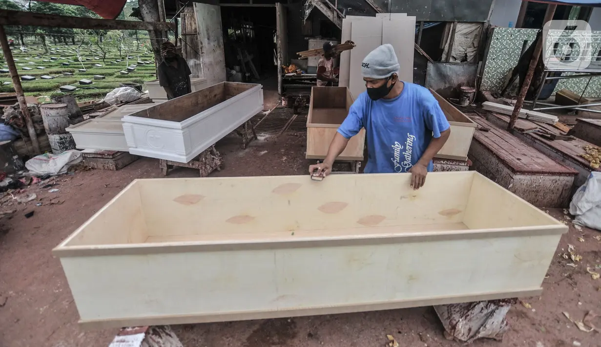 Pekerja menyelesaikan pembuatan peti jenazah di TPU Pondok Kelapa, Jakarta, Selasa (13/7/2021). Melonjaknya angka kematian Covid-19 di Ibu Kota beberapa hari terakhir, menyebabkan jumlah permintaan peti jenazah kembali meningkat hingga membuat pasokan bahan baku menipis (merdeka.com/Iqbal S Nugroho)