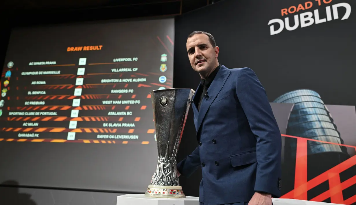 Mantan pemain sepak bola internasional Irlandia John O'Shea berpose di samping trofi kompetisi dan layar yang menampilkan jadwal pertandingan setelah pengundian babak 16 besar turnamen sepak bola Liga Europa 2023-2024 di House of European Football di Nyon, pada 23 Februari 2024. (Fabrice COFFRINI/AFP)