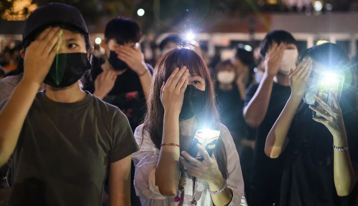 Mahasiswa menutup mata kanan mereka sambil menyalakan ponselnya selama rapat umum di Hong Kong (22/8/2019). para mahasiswa masih ingin memimpin barisan demonstran pro-demokrasi yang hampir setiap hari berada di jalanan untuk memberikan tekanan pada pemerintah. (AFP Photo/Anthony Wallace)