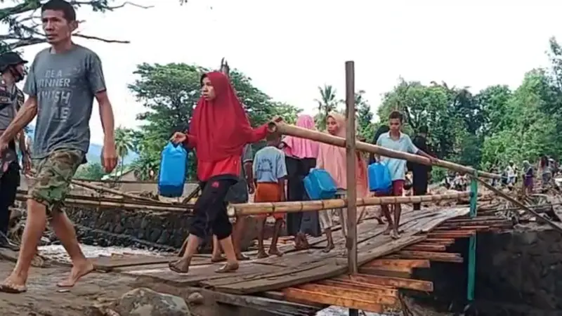 Warga Desa Waiburak, melintasi jembatan darurat yang dibangun TNI/Polri pasca banjir bandang untuk membelih minyak tana di Kelurahan Waiwerang. (Liputan6.com/Dionisius Wilibardus)