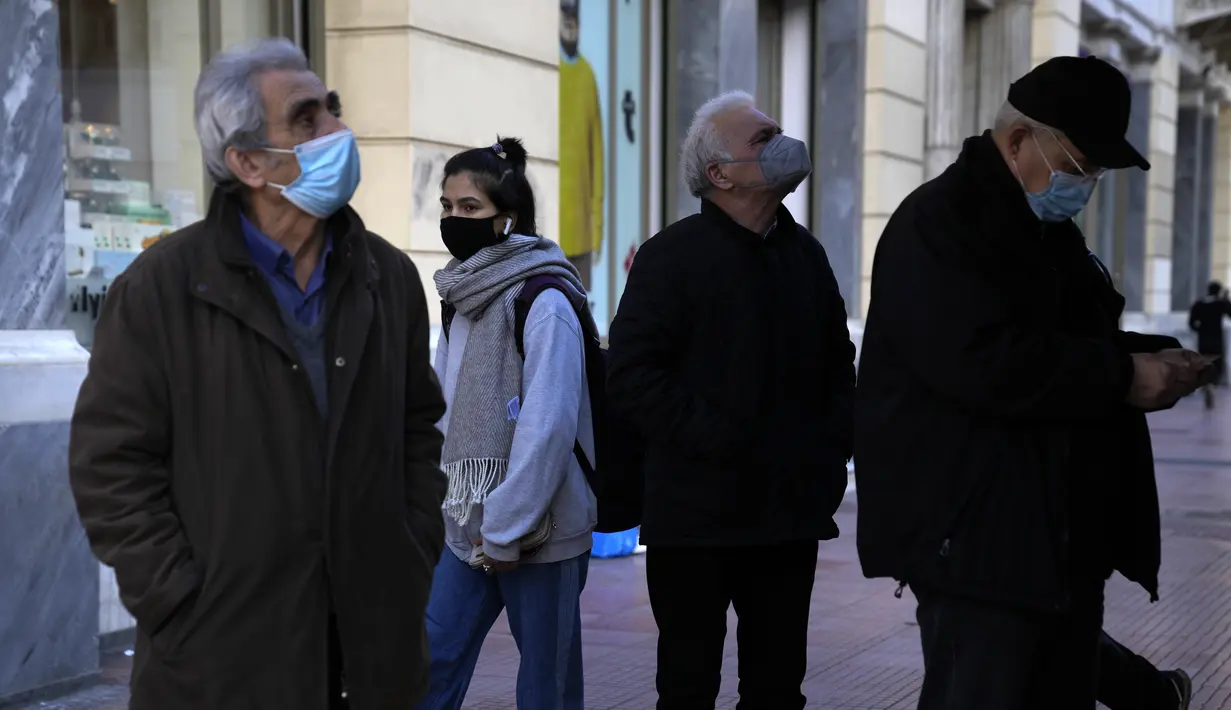 Dua pria lansia yang mengenakan masker membaca halaman depan surat kabar Yunani di Omonia square di Athena, Kamis (23/12/2021). Yunani membatalkan konser Natal dan acara lainnya sebagai bagian dari pembatasan baru yang mencakup mandat penggunaan masker di luar ruangan. (AP Photo/Thanassis Stavrakis