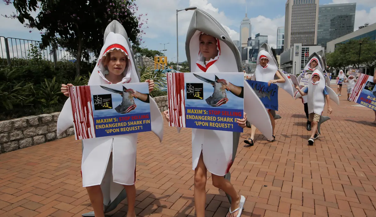 Sejumlah aktivis yang mengenakan pakaian hiu dan membawa poster saat menggelar aksinya di dekat restoran di Hong Kong (10/6). Aksi itu merupakan bagian dari protes mereka akan menu sirip hiu yang disajikan di restoran tersebut. (AP Photo / Kin Cheung)