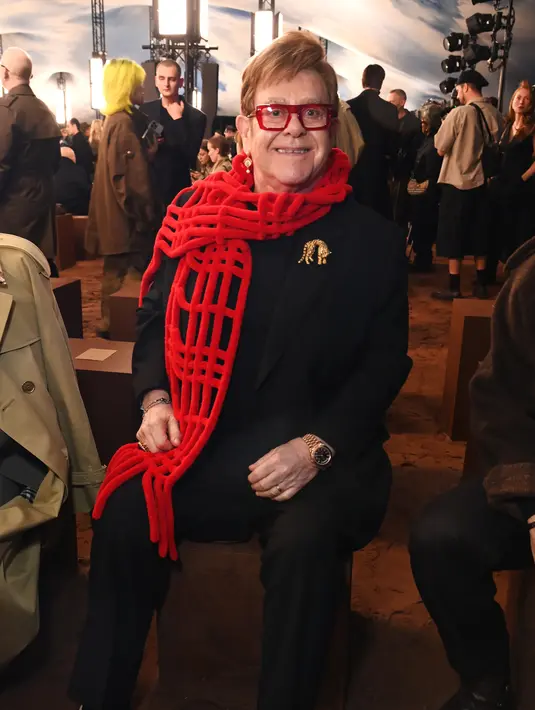 Elton John menjadi tamu yang ditunggu di gelaran show Burberry. Seperti biasa, ia kenakan setelan jas kasual dengan celana hitam dan sneakers. Tak ketinggalan syal rajut merah yang jadi aksesori ikonik [Burberry]
