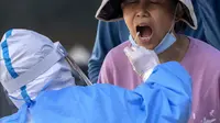 Seorang pekerja yang mengenakan pakaian pelindung menyeka tenggorokan seorang wanita untuk tes COVID-19 pada hari ketiga berturut-turut tes virus corona massal di Beijing, Kamis (5/5/2022). Ibu kota China Beijing pada Kamis (5/5) mulai melonggarkan aturan karantina untuk kedatangan dari luar negeri. (AP Photo/Mark Schiefelbein)