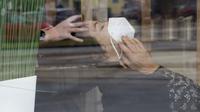 Terlihat dari kaca jendela, seorang perempuan dengan masker berada di salon rambut setelah pelonggaran lockdown di Wina, Austria, Senin (8/2/2021). Austria mulai melonggarkan lockdown covid-19 ketiga mereka dengan mengizinkan sekolah, museum dan toko dibuka kembali. (AP Photo/Ronald Zak)