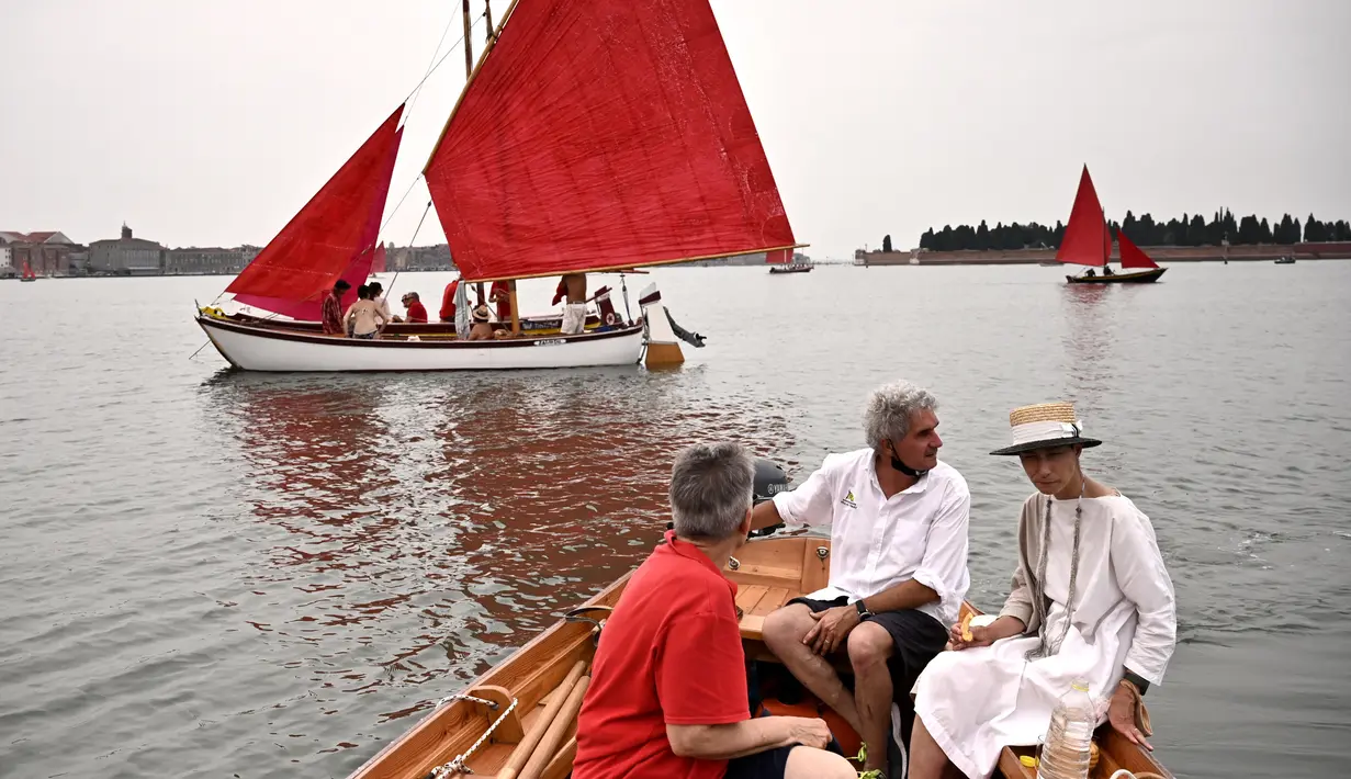 Anggota asosiasi pelayaran budaya mengambil bagian dalam acara Regatta Merah di Venesia, Italia, Minggu (20/6/2021). Regatta Merah diselenggarakan oleh seniman AS Melissa Mc Gill. (MARCO BERTORELLO/AFP)