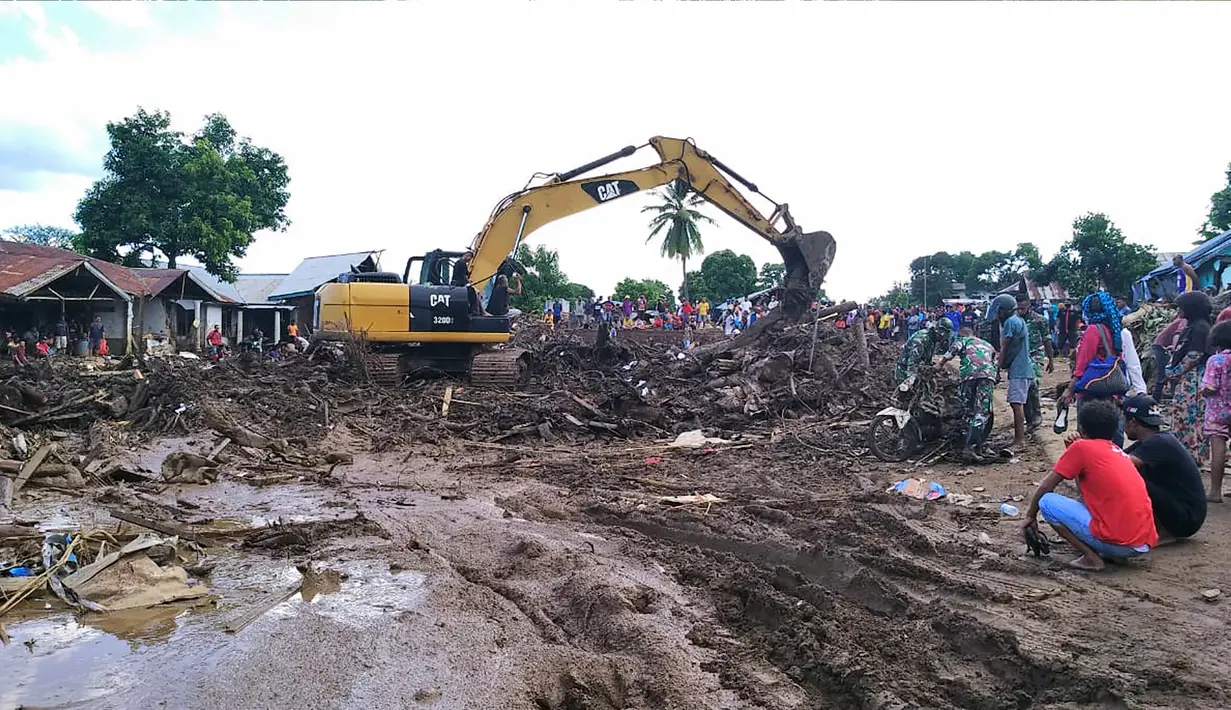 Warga menyaksikan ekskavator membersihkan puing pada daerah yang terkena banjir bandang di Waiwerang, Pulau Adonara, Nusa Tenggara Timur, Selasa (6/4/2021). Tim penyelamat terus menggali puing tanah longsor untuk mencari korban yang terkubur usai bencana banjir bandang. (AP Photo/Rofinus Monteiro)