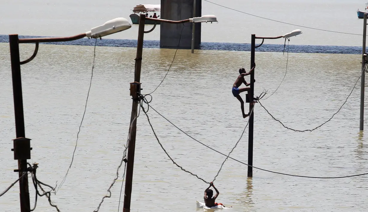 Warga memanjat tiang listrik saat terjebak banjir di tepi sungai Gangga, Allahabad, India, (21/8). Banjir bandang menerjang sejumlah wilayah di India yang menyebabkan banyak warga yang terjebak. (REUTERS/Jitendra Prakash)