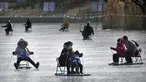 Seorang wanita dan anak-anak mendorong kursi es melintasi kolam beku di taman umum di Beijing, Selasa (17/1/2023). China telah mengumumkan penurunan populasi pertamanya dalam beberapa dasawarsa seiring bertambahnya usia negara terpadat di dunia dan angka kelahirannya yang menurun. (AP Photo/Mark Schiefelbein)