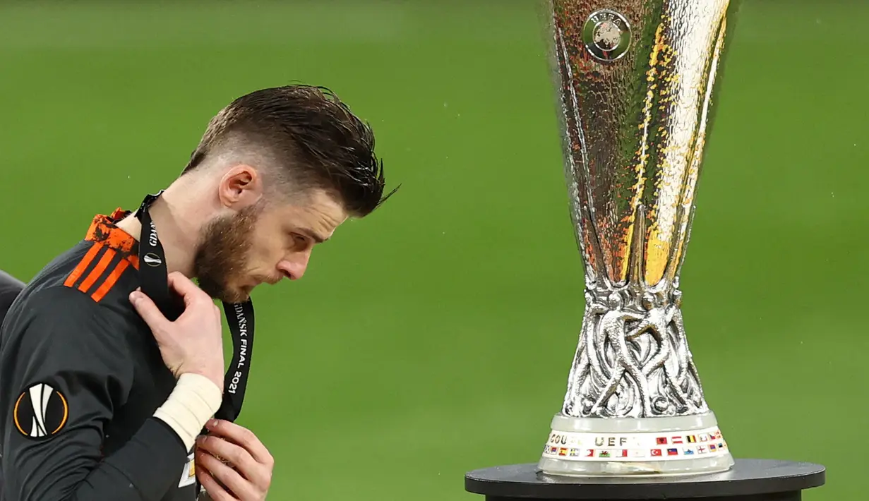 Reaksi kecewa kiper Manchester United, David de Gea saat berjalan melewati trofi Liga Europa 2020/2021 setelah dikalahkan Villarreal CF di Gdansk Stadium, Gdansk, 26 Mei 2021. Meskipun begitu, De Gea pernah mempersembahkan satu trofi Liga Europa untuk MU pada 2016/2017. Kala itu Setan Merah berhasil menang dengan skor 2-0 atas Ajax Amsterdam. (AFP/Pool/Maja Hitij)