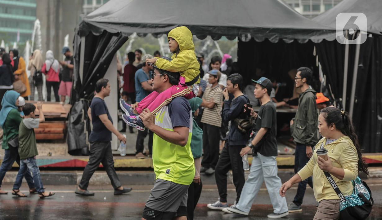 Warga menggendong anak kecil saat car free day (CFD) di kawasan Bundaran HI, Jakarta, Minggu (29/12/2019). Kendati tidak seramai saat cerah, warga yang berlari, jalan santai, atau swafoto masih menjadi pemandangan di area CFD usai hujan mengguyur Jakarta. (Liputan6.com/Faizal Fanani)