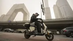 Seorang pria yang mengenakan masker mengendarai skuter di sepanjang jalan di kawasan pusat bisnis di Beijing, Rabu, 22 Maret 2023. (AP Photo/Mark Schiefelbein)