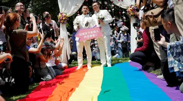 Pasangan sesama jenis berjalan di atas bendera pelangi raksasa saat melangsungkan pesta pernikahan mereka di Taipei, Taiwan, Jumat (24/5/2019). Taiwan menggelar pernikahan sesama jenis pertama di Asia. (REUTERS/Tyrone Siu)