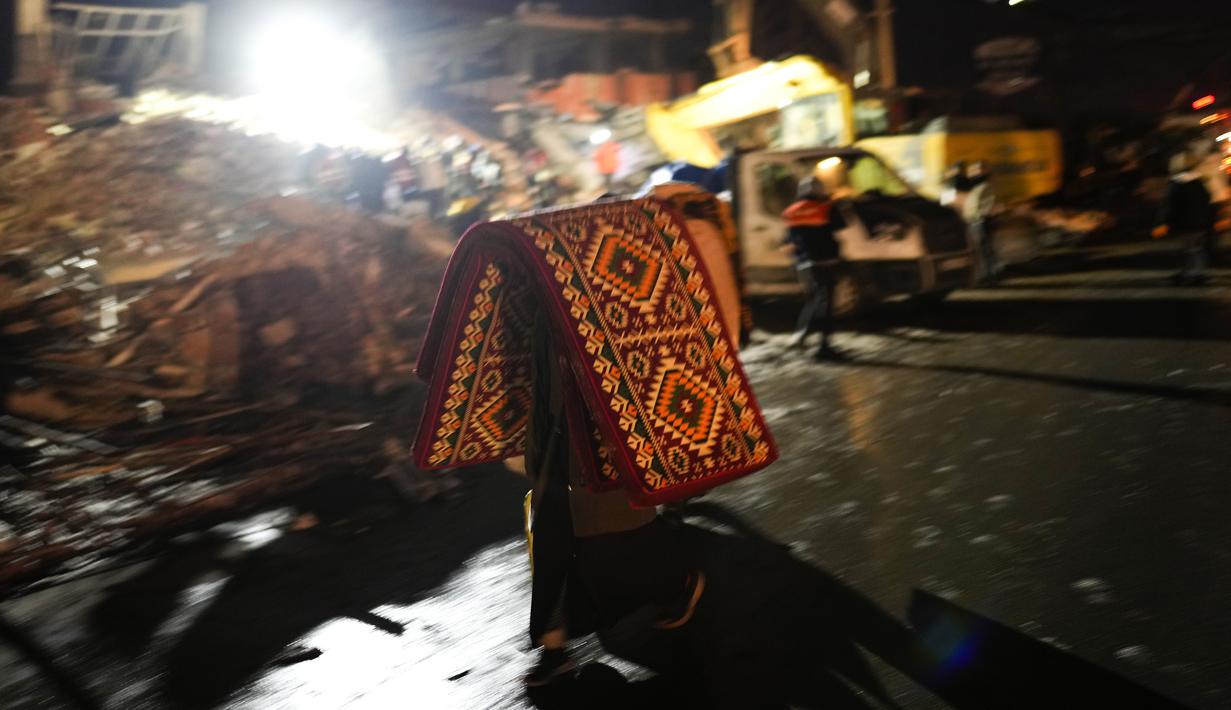 Seorang pria membawa selimut dan kasur saat tim penyelamat mencari korban gempa Turki di bangunan yang hancur di Elbistan, Turki selatan, Rabu, 8 Februari 2023. Tim penyelamat terkadang menggunakan ekskavator atau mengambil dengan hati-hati melalui puing-puing. Tidak jelas berapa banyak orang yang mungkin masih terjebak. (AP Photo/Francisco Seco)