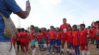Sejumlah anak peserta coaching clinic melakukan sesi foto bersama pemain asing Malut United, Mukhammad Isaev,&nbsp;di Stadion Gelora Kie Raha, Ternate, Minggu (13/8/2023) sore hari WIT. (Bola.com/Okie Prabhowo)
