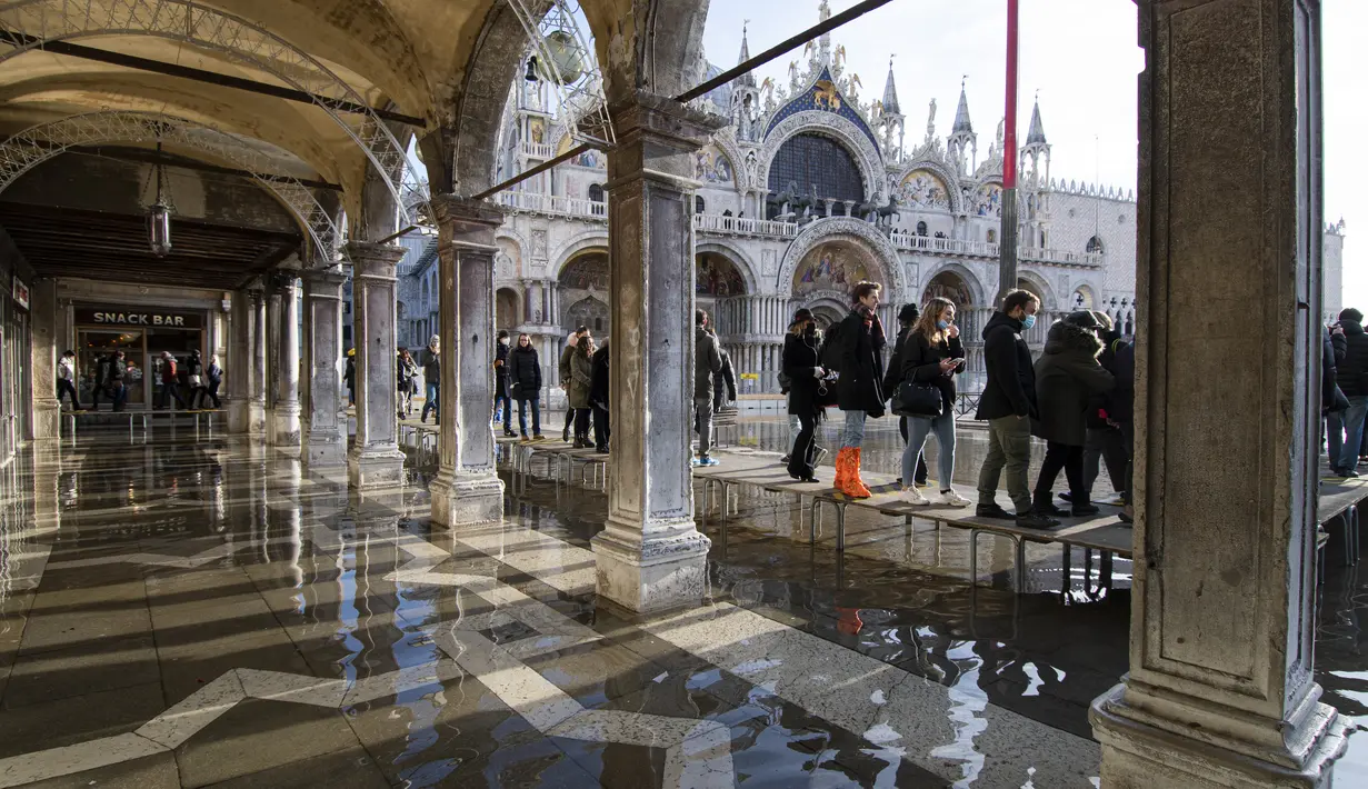 Orang menggunakan jembatan trestle untuk menyeberangi St Mark's Square yang dibanjiri air laut, di Venesia, Italia, Sabtu (4/12/2021). Air mencapai 99 sentimeter di atas permukaan laut dan bagian terendah kota tenggelam. (AP Photo/Luigi Costantini)