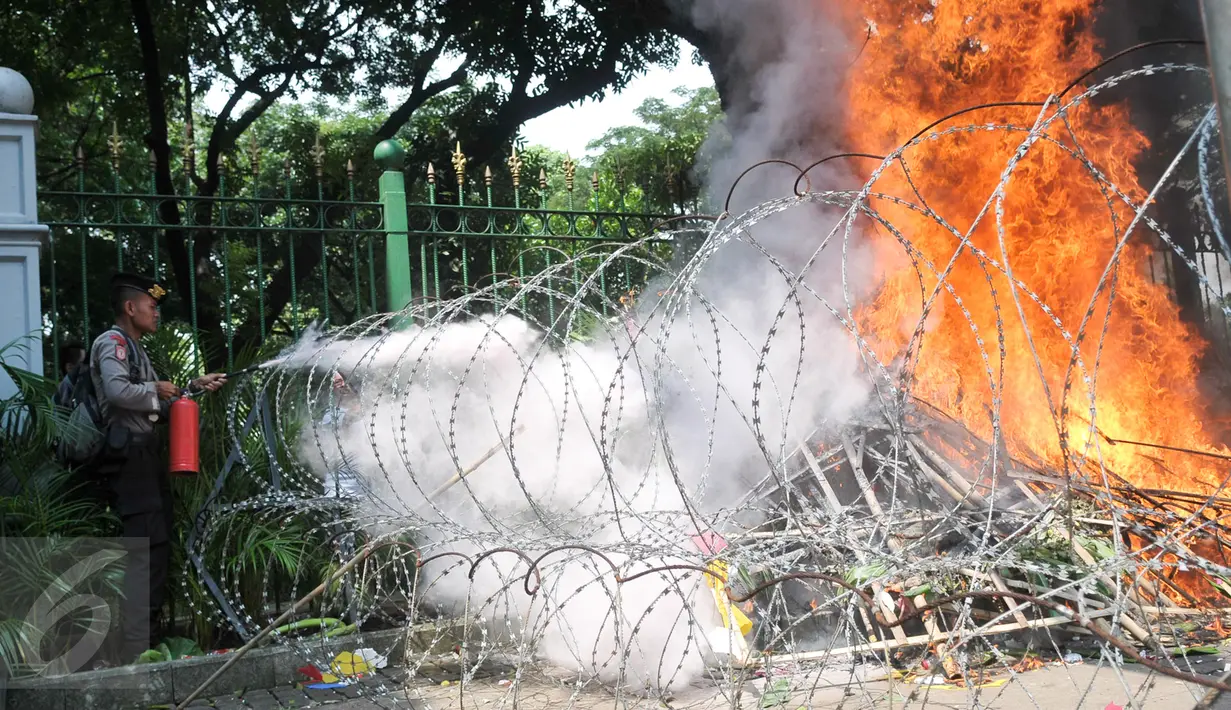 Polisi memadamkan karangan bunga yang dibakar oleh orang yang diduga menjadi provokasi saat aksi Hari Buruh di Jalan Medan Merdeka Barat, Jakarta, Senin (1/5). (Liputan6.com/Yoppy Renato)