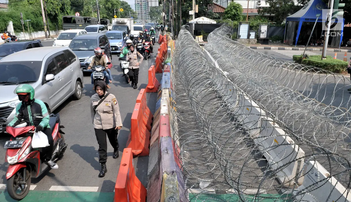 Aparat kepolisian melintasi kawat berduri yang memblokade jalan ke arah gedung KPU, Jakarta Pusat, Minggu (30/6/2019). Penjagaan gedung KPU diperketat menjelang rapat pleno terbuka penetapan pasangan calon presiden dan wakil presiden terpilih Pemilu 2019. (merdeka.com/Iqbal S Nugroho)