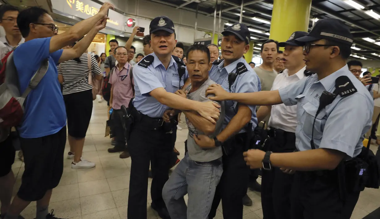 Polisi menahan  penumpang yang marah yang mencoba untuk bertarung dengan para pengunjuk rasa di Hong Kong, Selasa (30/7/2019). Para Pengunjuk rasa telah mengganggu layanan kereta bawah tanah pada pagi hari. (AP Photo/Vincent Yu)