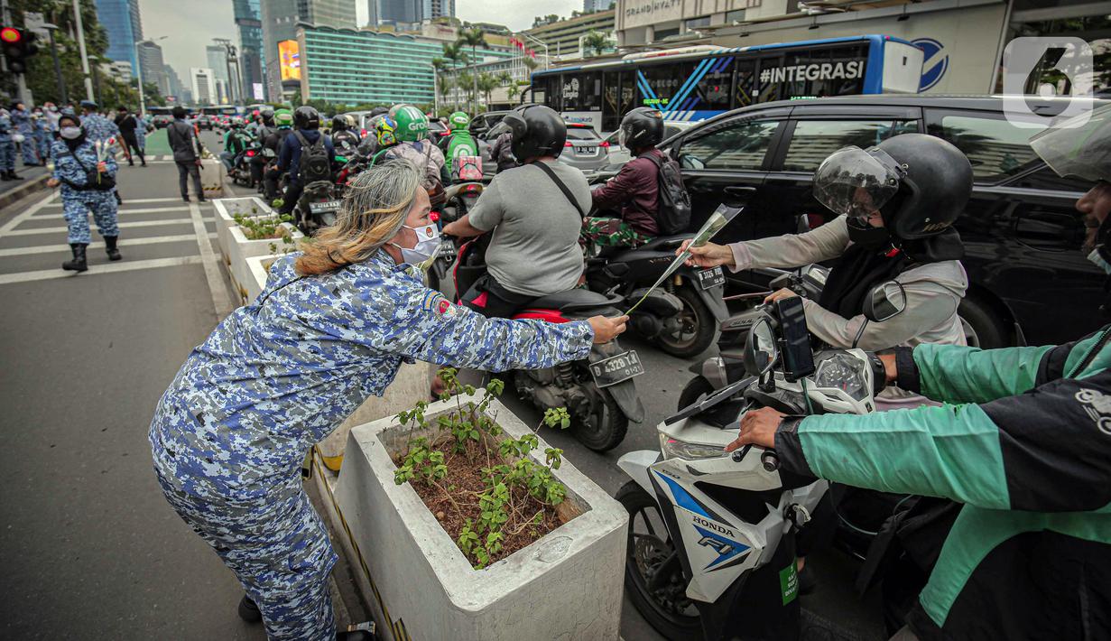 Perserta yang tergabung dalam Forum Kader Bela Negara DKI Jakarta membagikan bunga dan masker kepada pengguna jalan di Jalan Thamrin, Jakarta, Rabu (22/12/2021). Aksi tersebut merupakan bentuk apresiasi terhadap kaum perempuan terutama pada peringatan Hari Ibu. (Liputan6.com/Faizal Fanani)