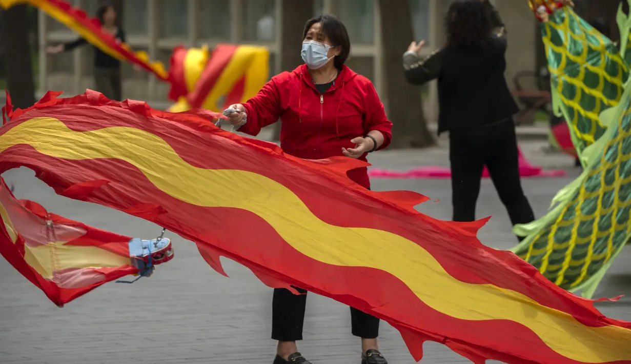 <p>Seorang wanita mengenakan masker mengibarkan bendera di taman umum di Beijing, Kamis (21/4/2022). Di daratan China, jumlah kematian meningkat menjadi lebih dari 20 dalam wabah di Shanghai yang menutup kota terbesar di negara itu. (AP Photo/Mark Schiefelbein)</p>