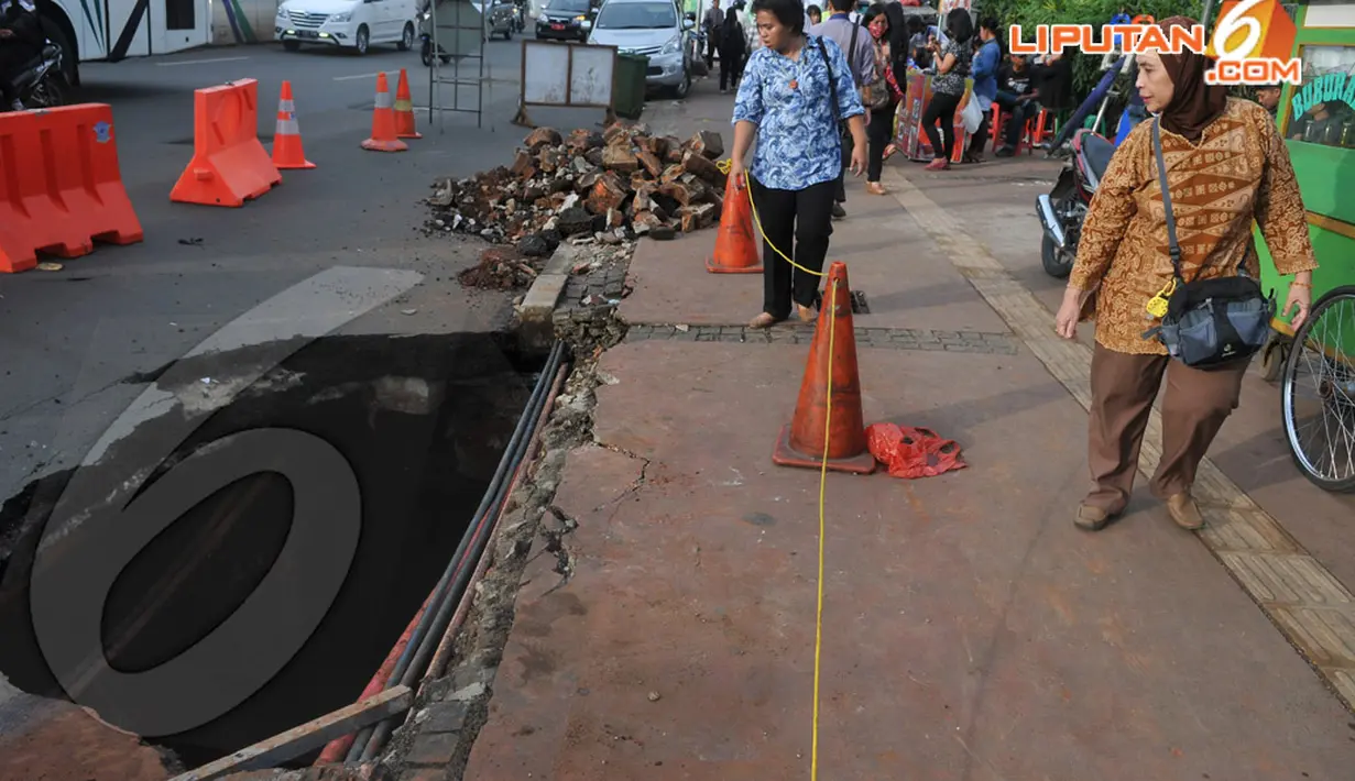 Dua orang wanita pejalan kaki tampak penasaran terhadap jalan yang amblas di kawasan Sudirman . Kamis (10/4/2014)  (Liputan6.com/Johan Tallo).