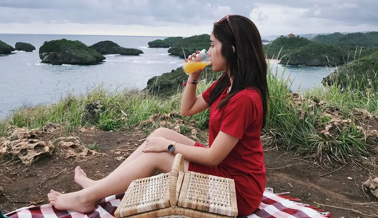 Fay Nabila tampak cantik dengan busana berwarna merah. Berpose di Pantai Kasap yang merupakan Raja Ampatnya Pacitan layaknya sedang piknik, ia tampak sedang minum jeruk dan menikmati indahnya suasana pantai tersebut. (Liputan6.com/IG/faynabilalxndr)