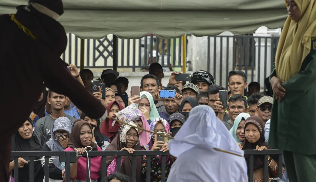 Warga menonton hukum cambuk yang dilakukan kepada Tjia Nyuk Hwa di luar Masjid Babussalam, Banda Aceh, Aceh, Indonesia, Selasa (27/2). Tjia Nyuk Hwa dicambuk sebanyak tujuh kali, sedangkan suaminya enam kali cambukan. (AFP FOTO/CHAIDEER MAHYUDDIN)