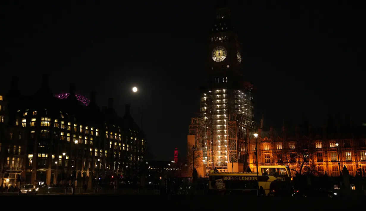 Bulan purnama pertama tahun ini atau Wolf Moon terlihat di belakang London Eye dan tampilan jam saat perbaikan Menara Elizabeth, yang dikenal sebagai Big Ben dan Gedung Parlemen, di London, Senin (17/1/2022). Wolf Moon adalah sebutan untuk bulan purnama pertama di Januari. (AP Photo/Matt Dunham)