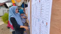 Salah satu warga RT 04 Palembang saat melihat papan nama-nama caleg di Pemilu 2024 (Liputan6.com / Nefri Inge)