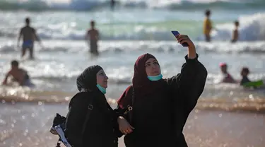 Wanita Palestina berselfie selama liburan Idul Fitri, di pantai laut Mediterania di Tel Aviv, Israel (25/5/2020).  Idul Fitri menandai akhir bulan suci Ramadhan, perayaan tiga hari yang biasanya menggembirakan telah berkurang secara signifikan karena pandemi coronavirus. (AP Photo/Oded Balilty)