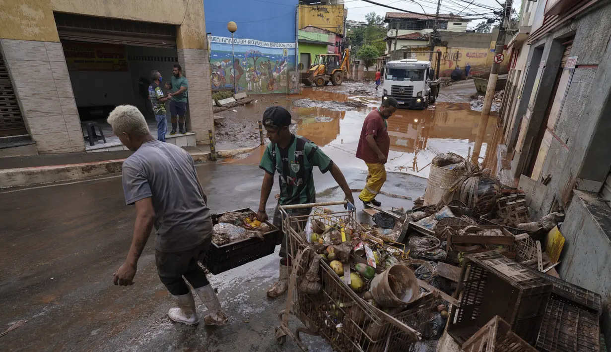 Warga memindahkan barang-barang yang rusak dan makanan busuk setelah banjir di Raposos, negara bagian Minas Gerais, Brasil (11/1/2022). Tanah longsor akibat hujan deras telah menewaskan sedikitnya 12 orang dan pihak berwenang sedang memantau bendungan yang bisa jebol. (AP Photo/Eugenio Savio)