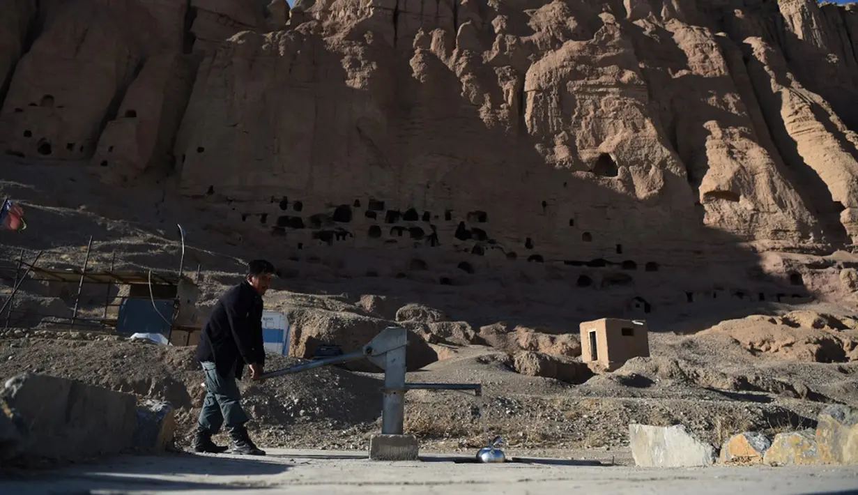 Seorang polisi Hazara mengumpulkan air dari pompa tangan dekat situs patung Buddha raksasa yang dihancurkan oleh Taliban pada 2001 di Provinsi Bamiyan, Afghanistan, 3 Maret 2021. Dua patung Buddha raksasa ini pernah dihancurkan oleh Taliban karena dianggap tidak Islami. (WAKIL KOHSAR/AFP)