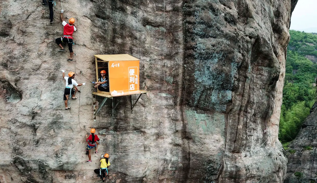 Sejumlah orang memanjat tebing melewati toko serba ada yang menempel di dinding tebing di Pingjiang di provinsi Hunan, China (25/4). Toko ini menjual minuman dan makanan untuk para pemanjat tebing yang melintas. (AFP Photo/China Out)