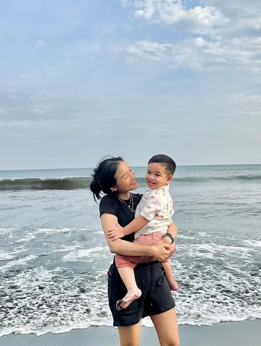Bermain di pantai, Fuji tampil kasual menggendong Gala. Ia mengenakan kaus hitam lengan pendek, dipadunya dengan celana pendek yang juga berwarna hitam. [Foto: Instagram/fuji_an]