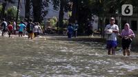 Warga melintasi genangan air yang merendam jalan di kawasan Kampung Makasar, Jakarta Timur, Senin (7/7/2025). (Liputan6.com/Herman Zakharia)
